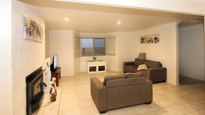 A living room with a fireplace, a sofa, a television, and a window with blinds.