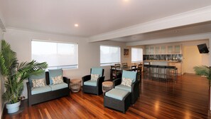 A spacious living area with wicker furniture, large windows, a kitchen area, and a dining table.
