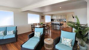Un vaste espace de vie comprenant un coin repas avec une table et des chaises, une cuisine à l’arrière-plan et une grande fenêtre laissant entrer la lumière naturelle.