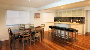 A dining area with a wooden table and chairs, a kitchen with white cabinets, and a bar area with stools.
