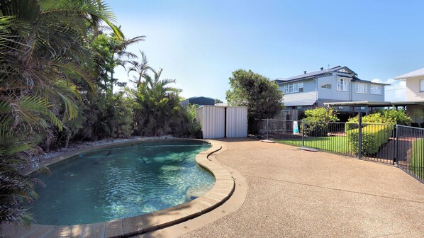 A swimming pool with a curved edge, surrounded by a gravel area and a metal fence.