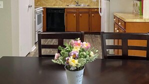 A kitchen with wooden cabinets, a white refrigerator, and a dining table with a floral centerpiece. - Huge Private 3 Bedroom House Large Master Fenced Yard, Galveston, Kemah, Fishing (Texas City)