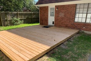 A wooden deck attached to a brick house with a door and window.