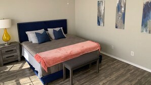 A bedroom with a bed, bedside table, bench, and abstract wall art. - Huge Private 3 Bedroom House Large Master Fenced Yard, Galveston, Kemah, Fishing (Texas City)