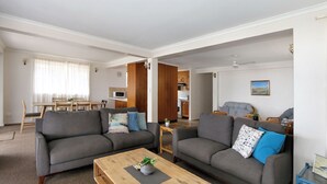 A modern living room with two grey sofas, a wooden coffee table, and a dining area with a table and chairs. - Horizons 3 & 3a/16 Miller Street Bargara (Bargara)