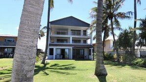 A two-story building with a balcony on the upper floor, surrounded by palm trees and a well-maintained lawn. - Horizons 3 & 3a/16 Miller Street Bargara (Bargara)