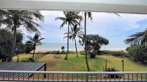 A view from a balcony overlooking a beach with palm trees and a bench. - Horizons 3 & 3a/16 Miller Street Bargara (Bargara)