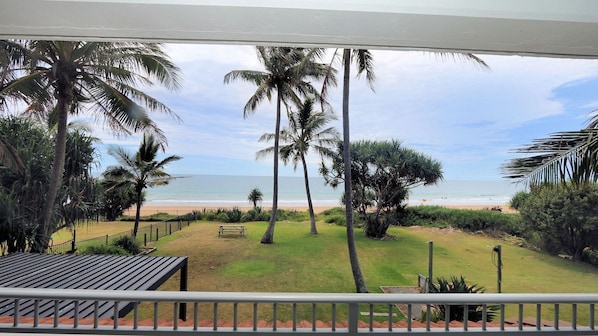 A view from a balcony overlooking a beach with palm trees and a bench.