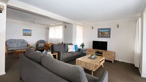 A modern living room with a grey sofa, a wooden coffee table, and a TV on a wooden stand. - Horizons 3 & 3a/16 Miller Street Bargara (Bargara)