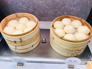 Dos vaporeras de bambú con bollos, una con la etiqueta 'bollo de verdura verde' y la otra 'bollo con carne'.