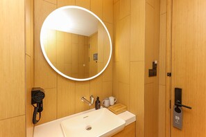A modern bathroom with a round mirror, a sink, a towel rack, a telephone, and a door with a handle.
