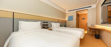 A hotel room with two beds, a desk, a chair, a trash bin, and a door leading to another room.