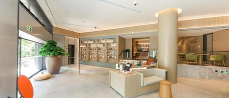 A modern hotel lobby with a reception desk, seating area, and a large plant.
