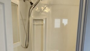 A bathroom with a white sink, a mirror, a shower, and a towel rack. - Hardy’s cute and cozy beach cottage  (Pointe-du-Chene)
