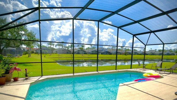 A covered swimming pool with a view of a green lawn and houses in the background. - Relaxing 4BR + 3Bath Villa Sleeps 10, with FREE heated pool!  (Kissimmee)