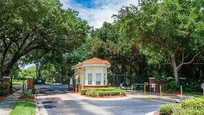 A gated entrance with a small building, surrounded by trees and a well-maintained lawn. - Relaxing 4BR + 3Bath Villa Sleeps 10, with FREE heated pool!  (Kissimmee)