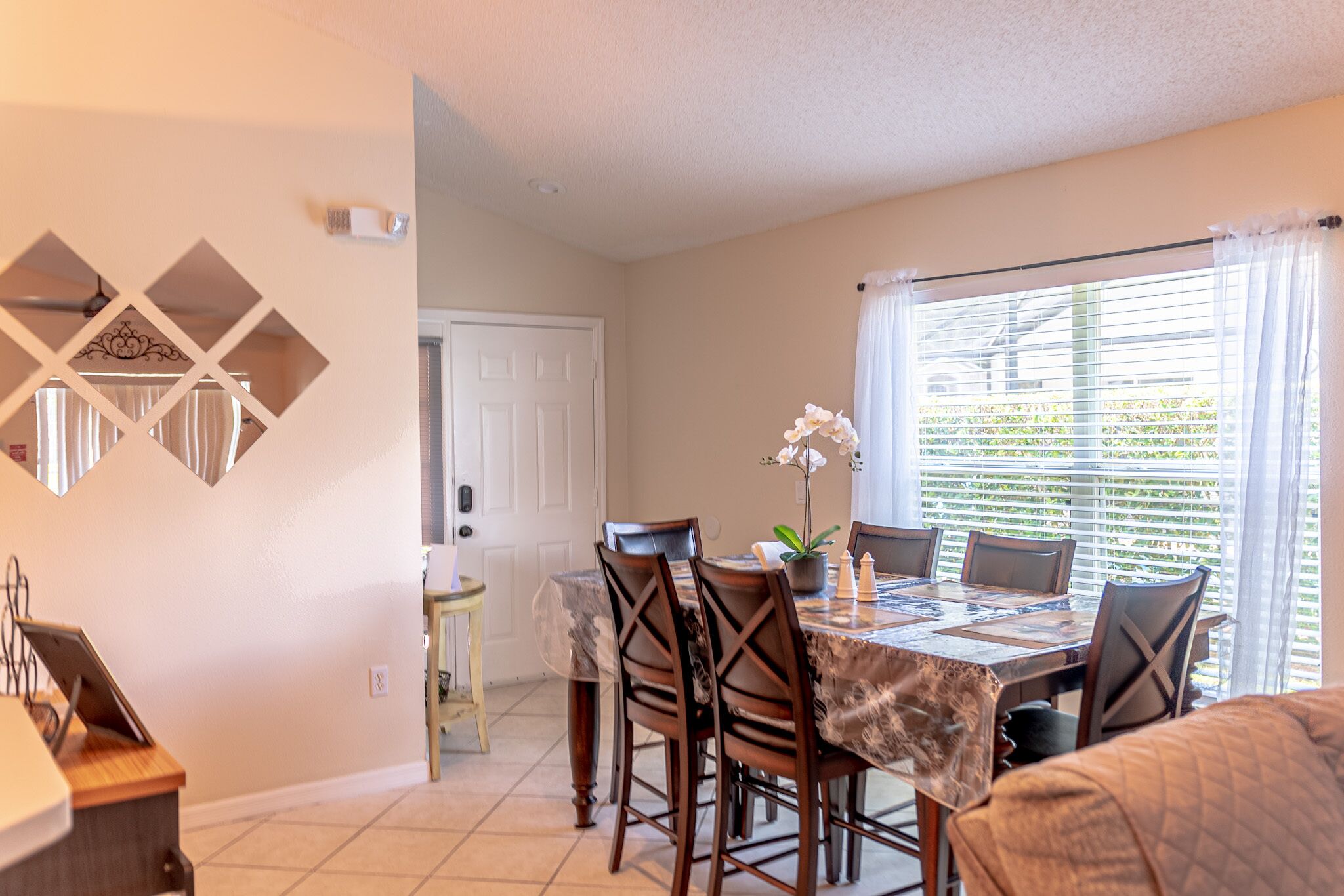 A dining area with a table set for four, surrounded by chairs, a potted plant, and a decorative wall piece.