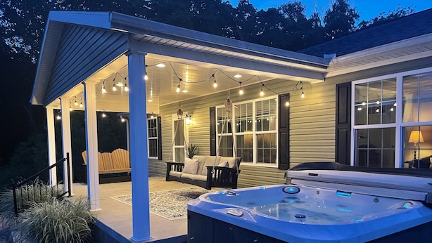 A hot tub in a covered outdoor area with string lights, a swing chair, and a patio table. - Natures Crest Retreat, Hocking Hills (Logan)
