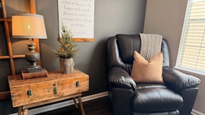 A cozy living room with a leather armchair, a wooden side table with a lamp, a decorative plant, and a motivational quote on the wall. - Natures Crest Retreat, Hocking Hills (Logan)