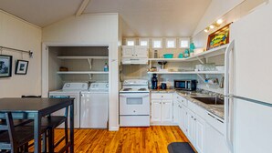 A compact kitchen with white appliances, a dining area with a table and chairs, and a wooden floor. - In Town, Pet Friendly, Golf Cart Accessible (Port Aransas)