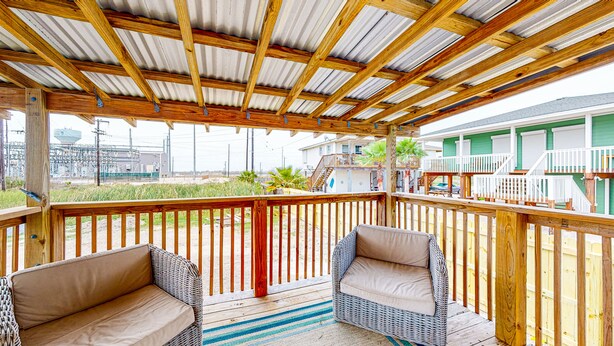 A covered outdoor deck with wicker furniture and a view of a residential area. - In Town, Pet Friendly, Golf Cart Accessible (Port Aransas)