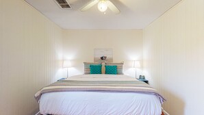 A neatly arranged bedroom with a bed centered, flanked by two bedside tables with lamps, a ceiling fan, and a wall-mounted artwork above the bed. - In Town, Pet Friendly, Golf Cart Accessible (Port Aransas)