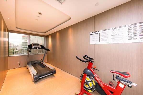 A gym with a treadmill and a stationary bike, a window with a city view, and a wall with informational posters. - Ji Hotel (Shanghai)