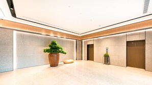 A modern lobby with a large potted plant, two elevators, and a polished marble floor.