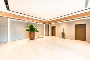A modern lobby with a large potted plant, two elevators, and a polished marble floor.