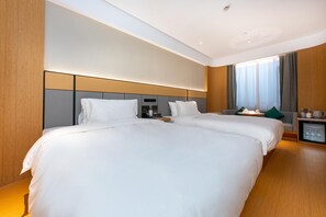 A hotel room with two beds, a small table with a lamp, a TV, and a window with curtains.