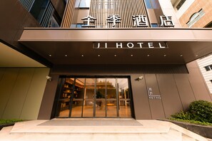 A modern hotel entrance with a glass door, signage for 'JI HOTEL,' and a visible outdoor seating area. - Ji Hotel (Shanghai)