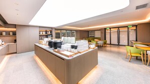 A modern hotel lobby with a central reception desk, seating area, and large windows.
