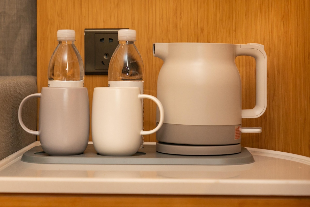 A tray with two mugs, a water bottle, and a coffee pot on a table.