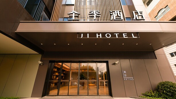 A modern hotel entrance with a glass door, signage for 'JI HOTEL,' and a visible outdoor seating area.