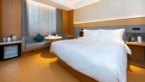 A modern hotel room with a large bed, a sofa, a small round table, and a minibar.