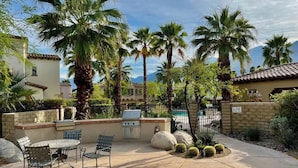 Patio esterno con barbecue, posti a sedere e palme.
