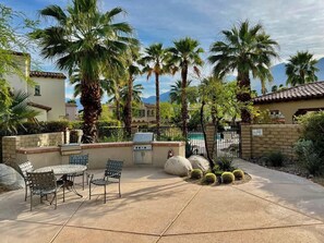 An outdoor patio with a grill, seating, and palm trees.