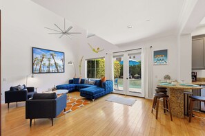 A modern living room with a sectional sofa, a dining area with bar stools, and a kitchen with a granite countertop.