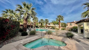 Una piscina con palme, un'area patio e un edificio sullo sfondo.