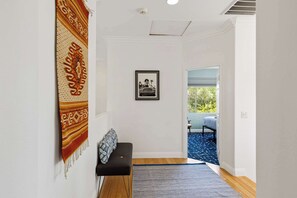 A hallway with a bench, a patterned rug, a framed picture, and a view into another room.