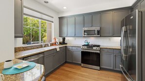 Una cucina moderna con mobili grigi, elettrodomestici in acciaio inossidabile, una finestra vista verde e un piano di lavoro in granito.