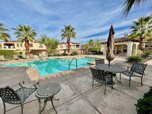 A pool area with lounge chairs and umbrellas, surrounded by palm trees and buildings.