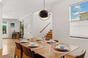 A dining area with a wooden table set for six, a staircase, and a view of the sky through a window.