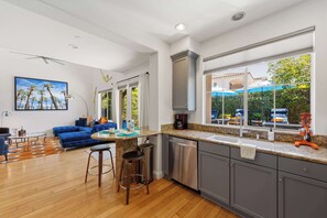 A modern kitchen with a built-in dishwasher, a dining area with a blue sofa, and a large window with a view of the outside.