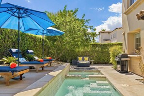 A pool area with lounge chairs, a blue umbrella, and a barbecue grill.