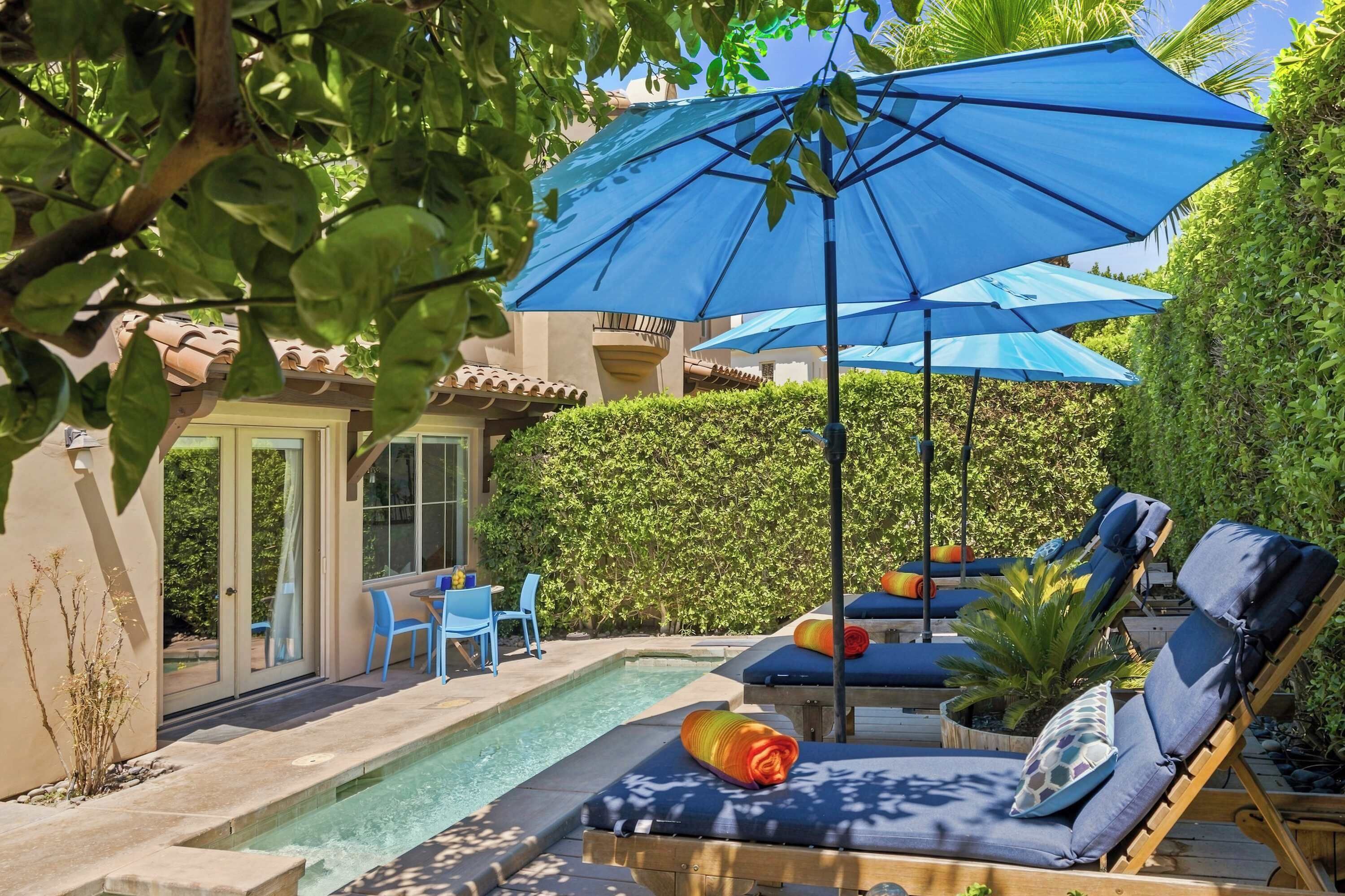 Zona junto a la piscina con sillones de descanso, sombrillas y una pequeña mesa.