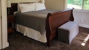 A bedroom with a wooden bed, a nightstand, a window, and three framed pictures on the wall.