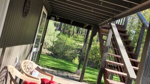 A covered outdoor area with a wooden deck, a staircase, and a view of a well-maintained lawn and trees.