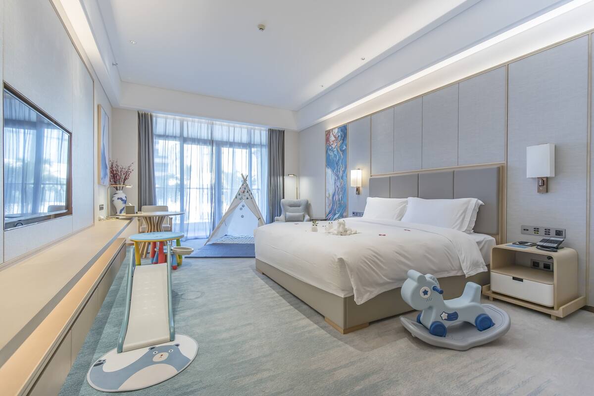 Een moderne hotelkamer met een groot bed, nachtkastje en een schommelpaard.