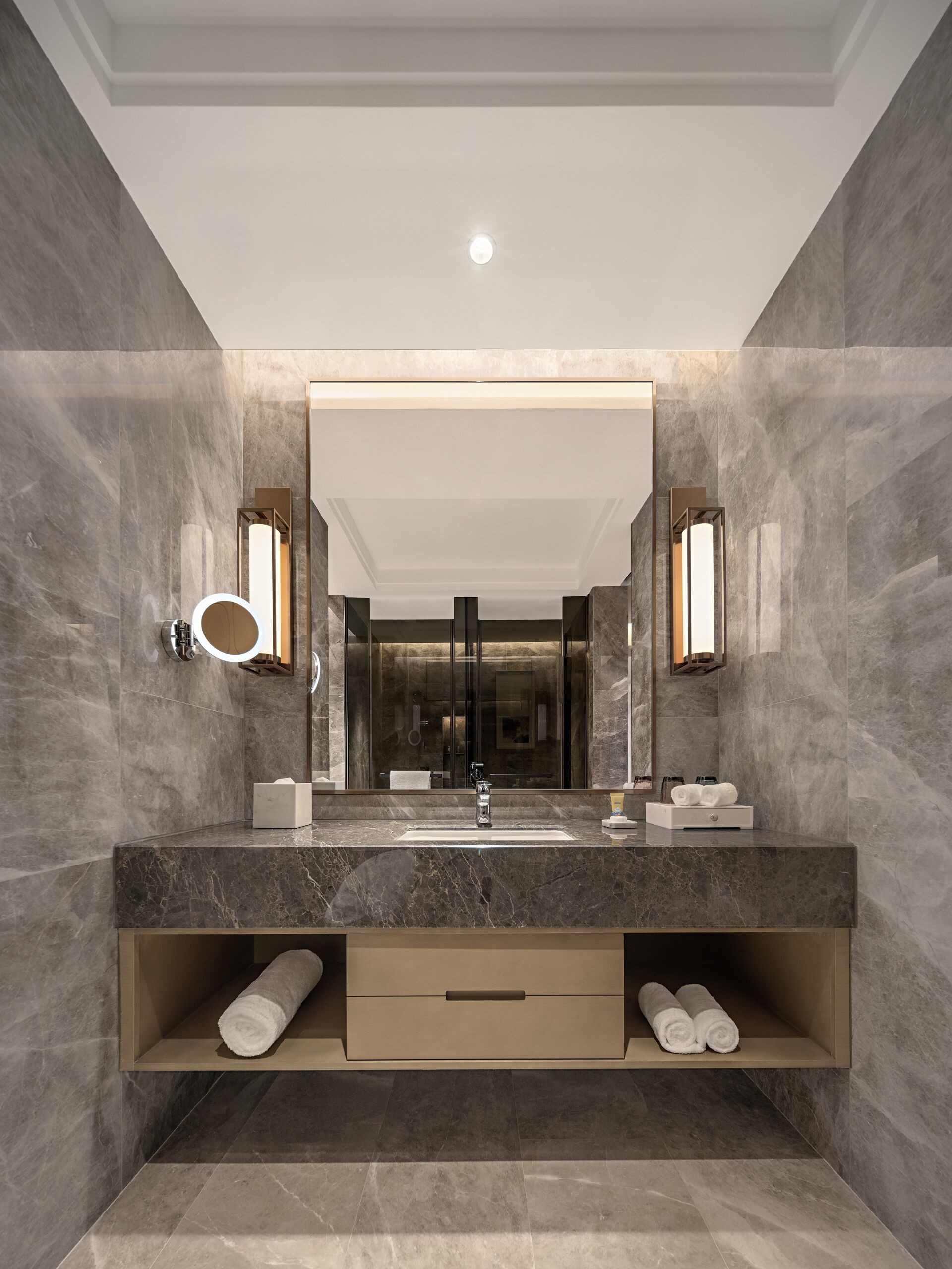 A modern bathroom with a large mirror, marble walls, and a built-in towel rack.